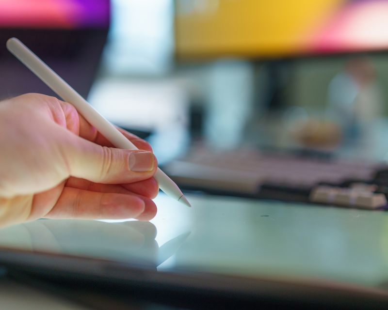 A hand marking up a screen layout with a stylus on a drawing tablet
