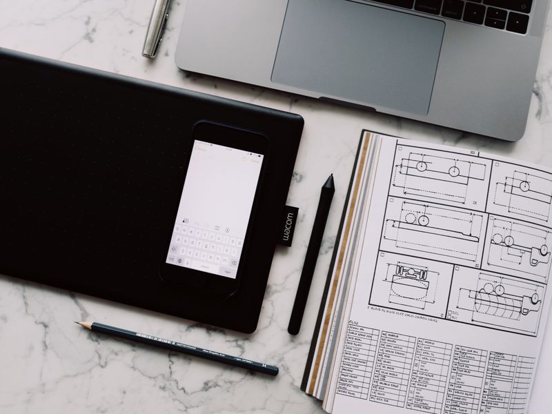 A tablet and printed wireframe sheets laid out on a desk from above