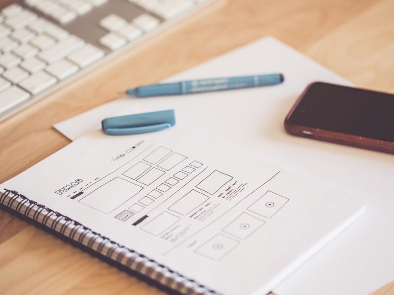 A notebook page of hand-drawn layout grids beside a pen and phone